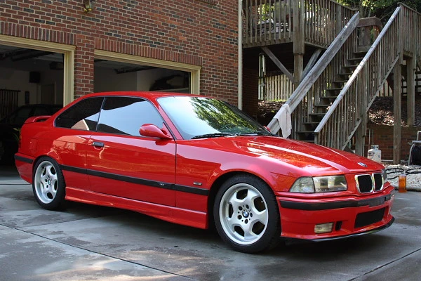 Red E36 M3 in a driveway outside a house